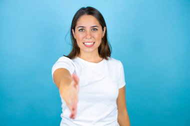 Soyutlanmış mavi arka plan üzerinde genç ve güzel bir kadın gülümseyerek selamlama ve karşılama olarak el sıkışmayı sunuyor.