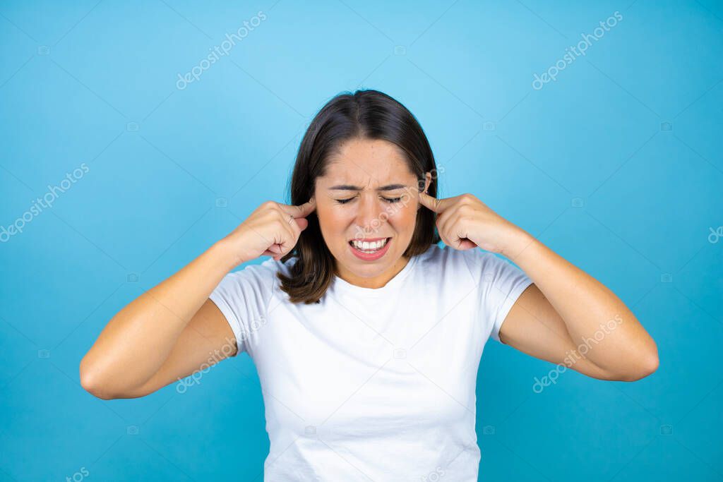 Young beautiful woman over isolated blue background covering ears with fingers with annoyed expression for the noise of loud music. Deaf concept.