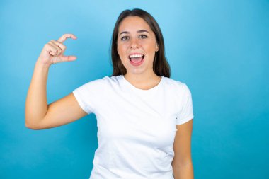 Genç ve güzel bir kadın, izole edilmiş mavi arka planda gülümsüyor ve el hareketleriyle hareket ediyor parmaklarıyla işaret ediyor ve kameraya bakıyor. Ölçü kavramı.