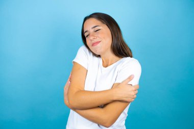 Genç ve güzel bir kadın soyutlanmış mavi arka planda kendine sarılıyor mutlu ve pozitif, kendine güvenen