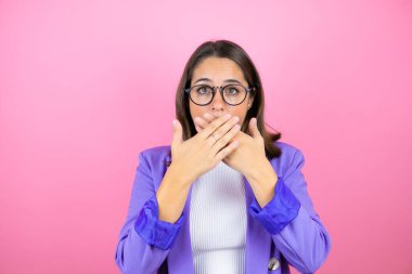 Soyutlanmış pembe arka planda genç ve güzel bir iş kadını ağzını yanlışlıkla ellerinle kapatarak şok etti. Gizli konsept.