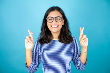 Gözlük takan güzel bir kadın mavi arka plan üzerinde durup umut dolu bir gülümsemeyle işaret ediyor..