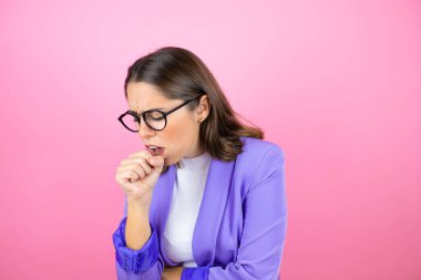 Genç ve güzel bir iş kadını pembe arka planda, eli ağzında, çünkü öksürüyor.