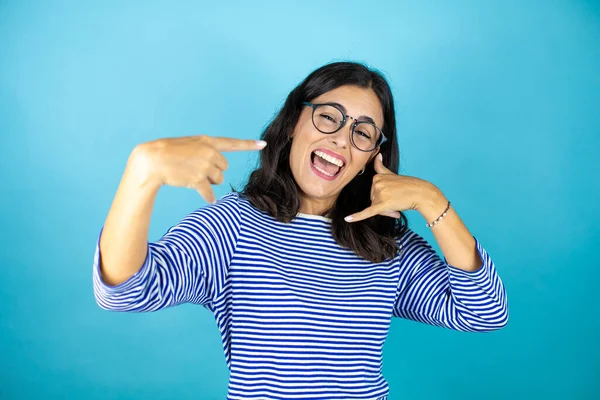 Gözlüklü güzel bir kadın mavi arka planda dikiliyor ve elleriyle bana jest yapıyor.