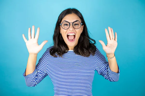 Gözlüklü güzel bir kadın mavi arka planda duruyor ve parmaklarını on numarayla gösteriyor ve gülümsüyor kendinden emin ve mutlu