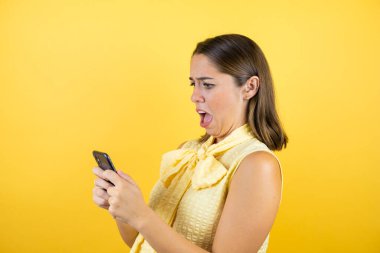 Soyutlanmış sarı arka planda genç ve güzel bir kadın telefonuyla konuşuyor ve şaşırıyor.