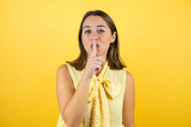 Soyutlanmış sarı arka planda genç ve güzel bir kadın sessiz olmak istiyor. Sessizlik ve gizli konsept.