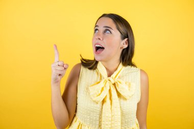Soyutlanmış sarı arka planda genç ve güzel bir kadın şaşırmış, işaret ediyor ve bakıyor..