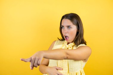 İzole edilmiş sarı arka plan üzerinde genç ve güzel bir kadın. Parmağı önde, ağzı açık, şaşırmış bir ifade. Ön tarafta bir şey var.