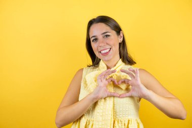 Genç, güzel bir kadın, izole edilmiş sarı bir arka planda gülümsüyor. Aşkla gülümsüyor.