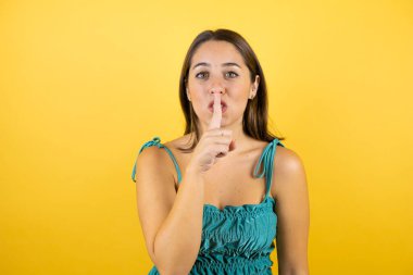 Soyutlanmış sarı arka planda genç ve güzel bir kadın sessiz olmak istiyor. Sessizlik ve gizli konsept.