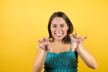 Genç, güzel bir kadın, izole edilmiş sarı arka planda gülümsüyor. Pençe hareketlerini kedi gibi yapıyor, agresif ve seksi bir ifade.