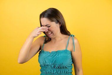 Güzel bir kadın, izole edilmiş sarı arka planda pis ve iğrenç bir koku alıyor. Nefesini burnunda tutuyor.