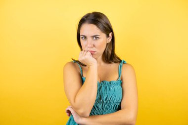 Soyutlanmış sarı arka planı olan genç ve güzel bir kadın çapraz kollardan sıkılmış ve yorgun göründüğünü düşünüyor.