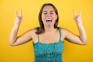 Sarı arka plan üzerinde genç ve güzel bir kadın çılgın bir ifadeyle el kaldırarak rock sembolü yapıyor.