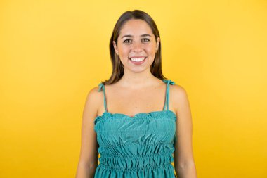 Genç ve güzel bir kadın, izole edilmiş sarı arka planda gülümsüyor ve kameraya bakıyor.