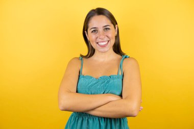 Sarı arka plan üzerinde kollarını kavuşturmuş gülümseyen güzel bir kadın.