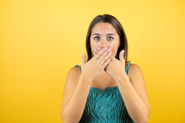 Young beautiful woman over isolated yellow background shocked covering mouth with hands for mistake. Secret concept.