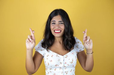 Sarı arka planda güzel bir kadın. Umut ve bakışıyla parmaklarını çapraz yapıyor.