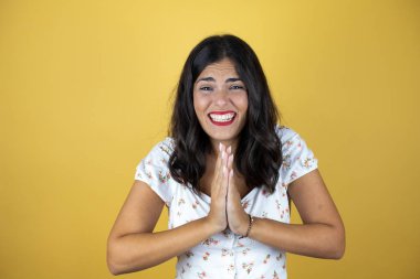 Sarı arka planda güzel bir kadın elleri bağlı yalvarıyor ve dua ediyor. Yüzünde umut ifadesi var. Çok duygusal ve endişeli.
