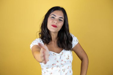 Sarı arka planda güzel bir kadın gülümseyerek selamlama ve hoş geldin demek için tokalaşıyor.