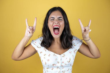 Sarı arka planda güzel bir kadın çılgın bir ifadeyle el kaldırarak rock sembolü yapıyor.