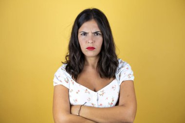 Sarı arka plan üzerinde güzel bir kadın şüpheci ve gergin, kollarını kavuşturmuş yüzünde onaylamayan bir ifade.