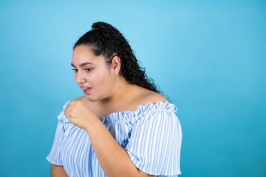 Kıvırcık saçlı, soyutlanmış mavi arka planı olan genç ve güzel bir kadın. Eli ağzında, çünkü öksürüyor.