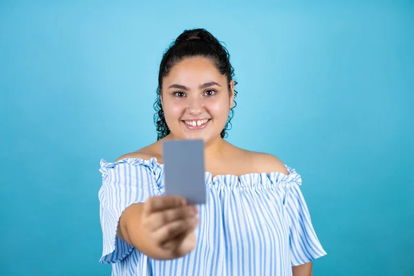 Young beautiful woman with curly hair over isolated blue background smiling and showing white card