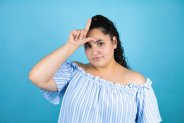 Mavi arka planda kıvırcık saçlı genç bir kadın. Alnında parmakları olan insanlarla dalga geçiyor. Ezik hareketler yapıyor, alay ediyor ve hakaret ediyor..