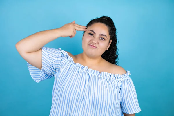 Kıvırcık saçlı, soyutlanmış mavi arka planda genç bir kadın. Kendini ve parmaklarını silah gibi gösterip öldürüyor. İntihar jesti..