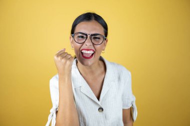 Sarı arka planda güzel bir kadın. Çok mutlu ve heyecanlı. Kollarını kaldırmış, gülümseyen ve başarı için çığlık atan kazanan bir jest yapıyor..