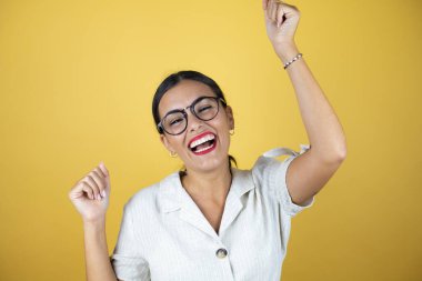 Sarı arka planda güzel bir kadın. Çok mutlu ve heyecanlı. Kollarını kaldırmış, gülümseyen ve başarı için çığlık atan kazanan bir jest yapıyor..