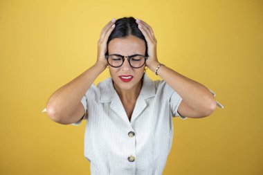 Sarı arka plan üzerindeki güzel kadın baş ağrısı ve stresten muzdarip çünkü elleri başının üstünde acı ve migren var.