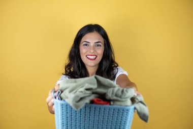 Sarı arka planda güzel bir kadın elinde sepetle ev işi yapıyor.