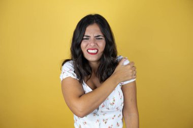 Omzunda ağrı ve acı dolu bir ifadeyle sarı arka planda güzel bir kadın.