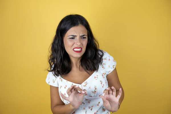 Beautiful woman over yellow background disgusted expression, displeased and fearful doing disgust face because aversion reaction. With hands raised. Annoying concept