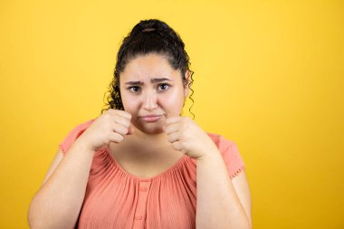 Sarı arka plan üzerinde kıvırcık saçları olan genç ve güzel bir kadın üzgün ve endişeli, sinirli ve korkmuş. Üzücü ifade.