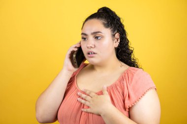 Genç, kıvırcık saçlı, izole edilmiş sarı arka planda endişeli bir ifadeyle genç bir kadın.