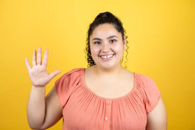 Sarı arka planda kıvırcık saçları olan genç ve güzel bir kadın beş numaralı parmaklarıyla gülümseyerek kendinden emin ve mutlu olduğunu gösteriyor.