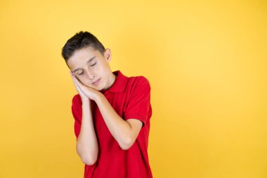 Genç, güzel bir çocuk, izole edilmiş sarı arka planda uyur, yorgun düşler kurar, elleriyle poz verir ve gözleri kapalı gülümserdi..