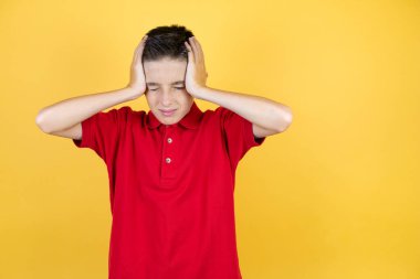 Güzel bir çocuk, sarı arka planda, baş ağrısı, çaresiz ve stresli bir şekilde acı çekiyor çünkü elleri başının üstünde migren ve acı çekiyor.