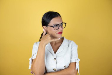 Sarı arka planda güzel bir kadın telefonla el ve parmaklarıyla jest yapıyor. Telefonda konuşur gibi.