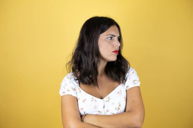 Sarı arka planda güzel bir kadın kollarını kavuşturmaktan yorgun ve sıkılmış göründüğünü düşünüyor.