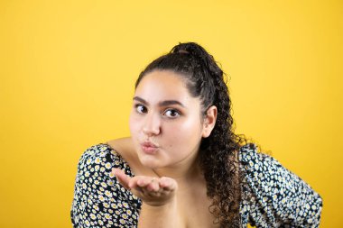 Sarı arka plan üzerinde kıvırcık saçları olan genç ve güzel bir kadın havayla öpüşürken kameraya bakıyor. Güzel ve seksi. Aşk ifadesi.