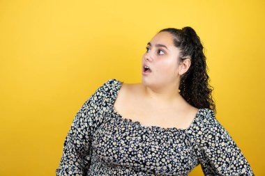 Sarı arka plan üzerinde kıvırcık saçları olan genç ve güzel bir kadın. Şaşırtıcı bir ifade, korku ve heyecanlı bir yüz ifadesiyle korkmuş ve şok olmuştu..