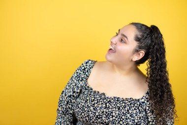 Sarı arka plan üzerinde kıvırcık saçlı, gülümseyen ve bakan güzel bir kadın.