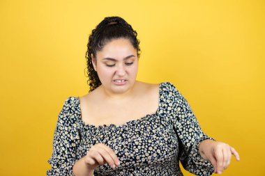 Sarı arka plan üzerinde kıvırcık saçları olan genç bir kadın tiksindirici tepki verdiği için tiksindirici ve tiksindirici bir ifade takındı. Eller havada. Can sıkıcı bir kavram.