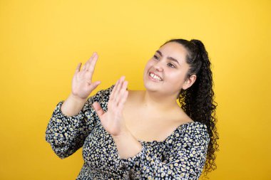 Sarı arka plan üzerinde kıvırcık saçları olan genç ve güzel bir kadın. Kolları yukarıdan düşmüş gibi korkmuş.