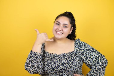 Kıvırcık saçlı, izole edilmiş sarı arka planda gülümseyen, el ve parmaklarıyla telefonla konuşan güzel bir kadın.